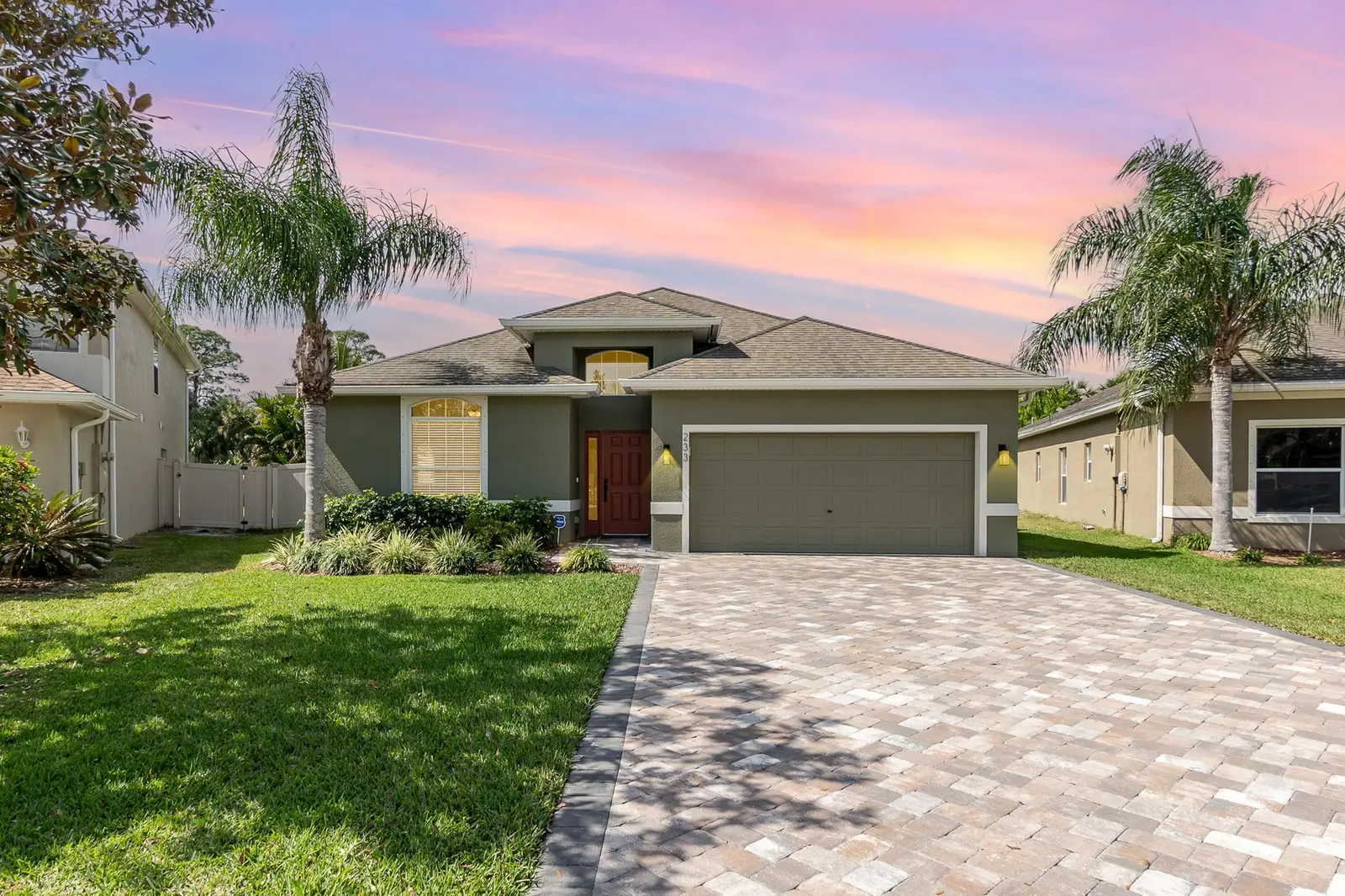 Single-family home with a paver driveway and palm trees at sunset